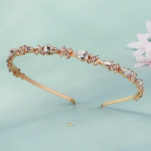 Elegant gold headband with sparkling round and pear-shaped crystals on a light blue background