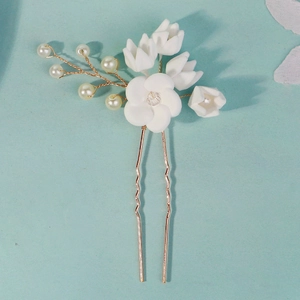 Macro detail of handmade white clay flowers and pearls on a gold U-shaped bridal hair pin