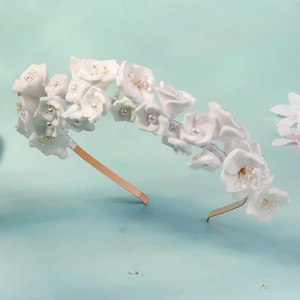 Détail de fleurs en tissu blanc avec perles sur un serre-tête de mariée en métal doré