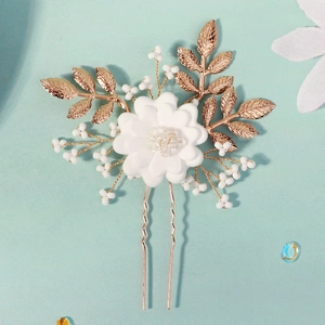 Detailed close-up of handmade white clay flower hair pin with golden leaves and pearls