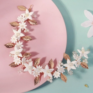 Detailed close-up of golden leaf headband with white ceramic flowers and pearls
