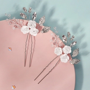 Macro detail of handmade white ceramic flower hair pins with crystals and silver leaves