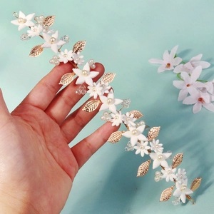 Detail of bridal headband with gold leaves, white fabric flowers and pearls decor