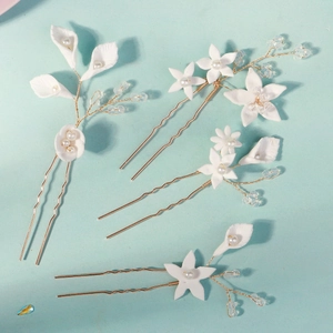 Macro detail of handmade U-shaped hairpins with white clay flowers and pearls on gold wire