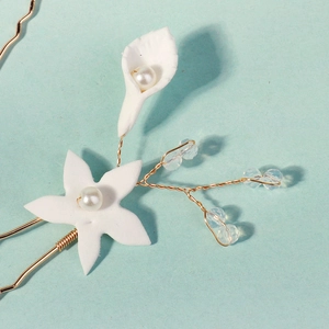 Close-up of handmade white clay flowers and pearls on a gold bridal hairpin detail