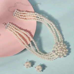 Detail of four-layer pearl necklace and flower earrings set with rhinestones on pink tray