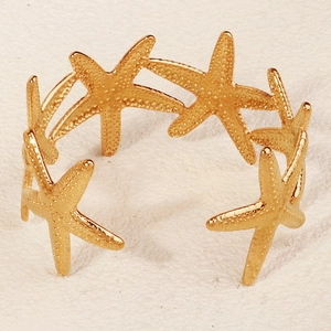 Detailansicht eines goldenen Seestern-Armreifs mit Textur auf sandigem Grund