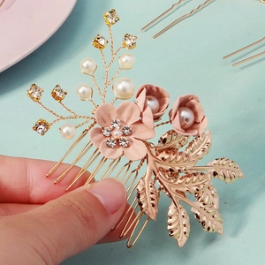 Détail de fleurs en tissu rose avec perles et feuilles dorées sur un peigne de mariée