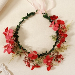 Close-up of artificial red floral headband with green leaves and pink ribbons on beige texture
