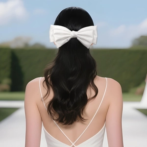Detail of a large white satin bow hair clip on long wavy hair for wedding hairstyle