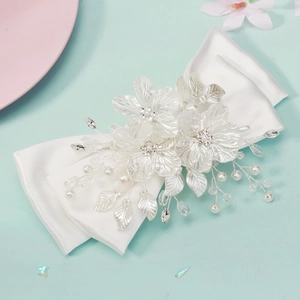 Close-up of white bridal hair clip with satin bow, floral elements, pearls and crystals