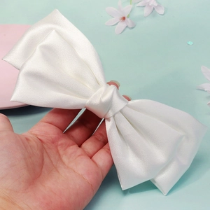 Close-up of a large white satin bridal bow hair clip held by hand to show its scale