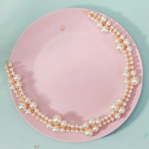 Close-up of handmade bridal headband with white pearls and gold wire on pink plate
