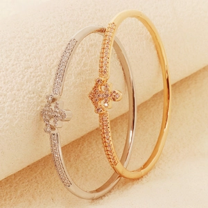 Macro detail of gold and silver bangles with crystal cross crowns on a textured stand