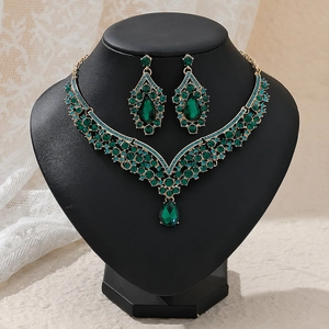 Detail of luxury gold jewelry set featuring green crystals and vintage V-shape necklace