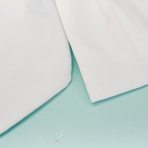 Detail of white bridal fabric with fine texture and a sparkling teardrop rhinestone accent