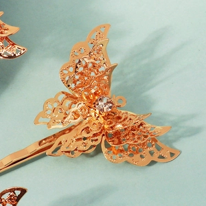 Detailed close-up of golden butterfly hair clip with hollow filigree and sparkling rhinestone