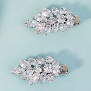 Detail of two silver leaf-shaped hair clips with shimmering zircon crystals on blue background