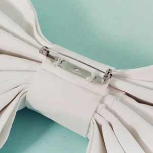Detail of the back side showing silver metal safety pin on the large white fabric bow
