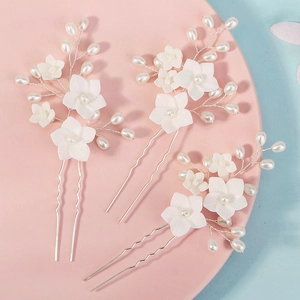 Close-up of bridal hair pins with white resin flowers and pearls on a pink plate