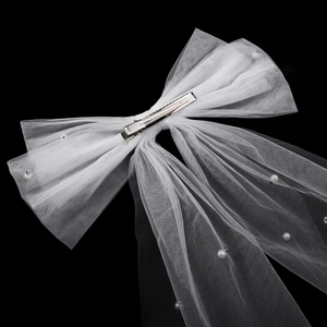 Detail of white mesh bridal bow with pearls and a metal alligator clip on black background