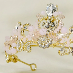 Close-up of pink crystal bridal crown with golden scrollwork and teardrop diamond