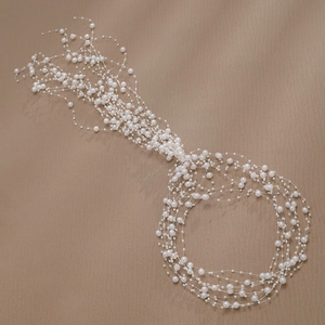 Detail of handcrafted white bridal hair vine with multi-layered pearls on a brown background