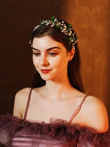 Detail of bridal headband with pearls, golden wire and green leaves on violet dress