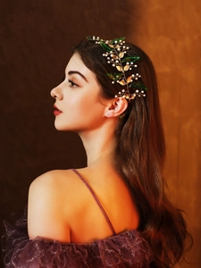 Detail view of gold vine headband with green acrylic leaves and pearls on a model