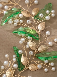 Macro view of gold bridal headband with acrylic green leaves and white pearls