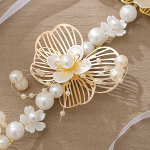 Détails de pétales dorés et perles blanches sur un bandeau de mariée avec rubans