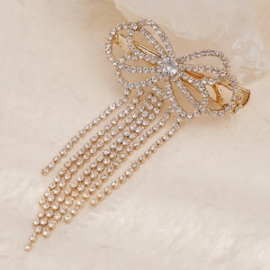 Elegant gold bow hair claw clip with sparkling rhinestone tassels on stone surface