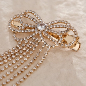 Close-up of golden rhinestone bow hair clip with dangling tassel on marble background