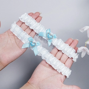 Detailed close-up of white ruffled bridal garter with blue heart rhinestones and bows