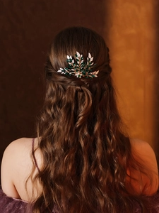 Close-up of elegant gold leaf hair comb with green gems and pearls on dark wavy hair
