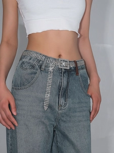Détail d'une ceinture de luxe avec strass portée sur un jean et un haut blanc