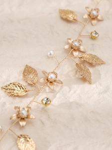 Détail de vigne de cheveux de mariée avec feuilles dorées, perles et strass sur papier beige