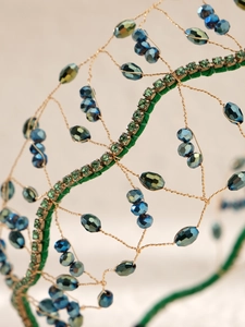 Détail macro d'un serre-tête baroque fait main avec cristaux vert forêt et fils dorés