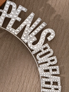 Macro view of crystal encrusted letters QUEEN on silver headband for party outfits