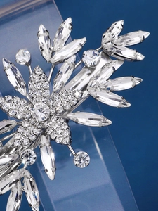 Macro shot of silver-toned flower hair clip with sparkling crystals on blue background