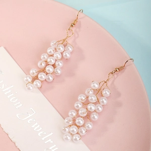Detailed macro view of bridal pearl drop earrings featuring a gold woven grape cluster design