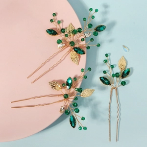 Detailed macro view of three handmade gold leaf hairpins with emerald green rhinestones