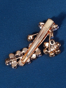 Macro detail of gold flower hair clip with sparkling rhinestones on navy background