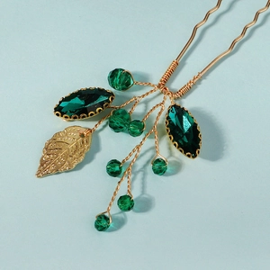 Detailed close-up of golden leaf pendant and green marquise gemstones on bridal hair pin