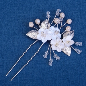 Handmade bridal hair pin with white clay flowers, crystals, and gold leaves on blue background