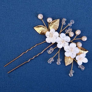Macro view of handmade white flower hair pin with gold leaves, crystals and pearls