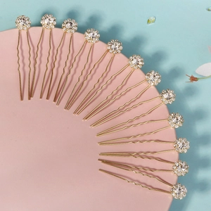 Détail de 15 épingles à cheveux dorées avec fleurs en strass disposées sur un support rose