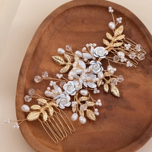 Handmade bridal hair comb with gold leaves, white flowers and pearls on wooden tray
