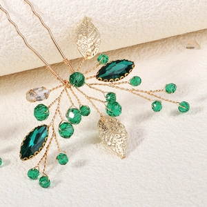 Macro detail of handmade bridal hair pins featuring gold leaves and green crystals