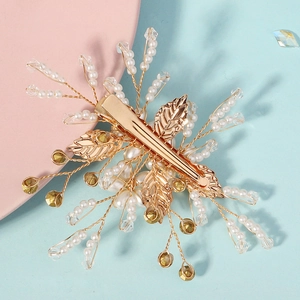 Elegant handmade pearl bridal hair clip with crystals and gold leaf details on pink background